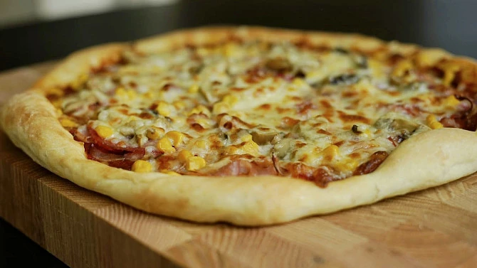 Připravená pizza s kynutým těstem na dřevěné desce
