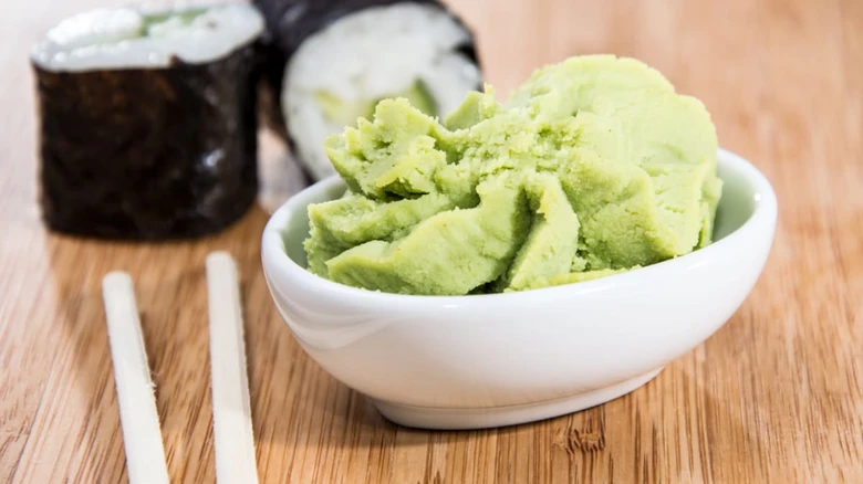 Čerstvá zelená pastová wasabi v bílé misce vedle rýžových rolí.
