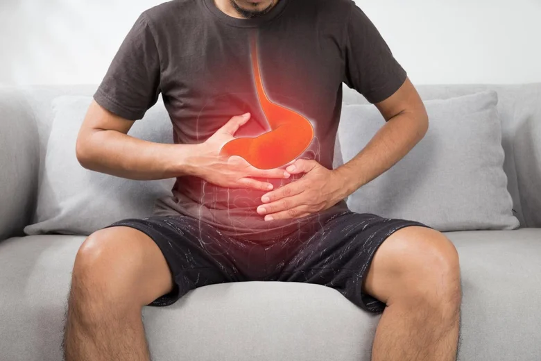 Muž s bolestí břicha ukazující na žaludek při refluxu.