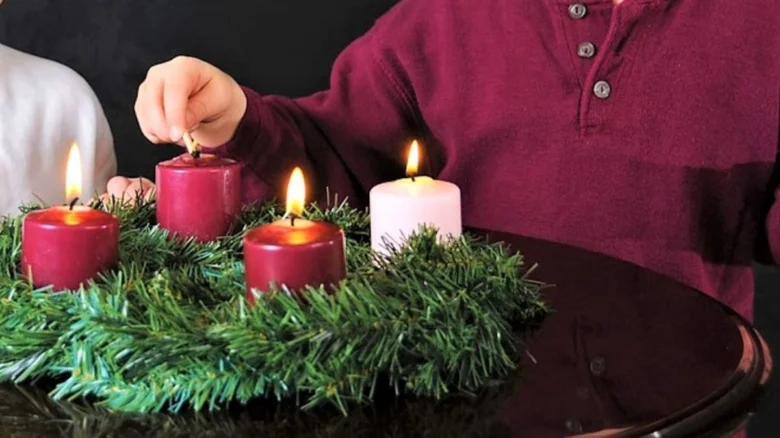 Dítě zapaluje svíčku na adventním věnci s třemi hořícími svíčkami