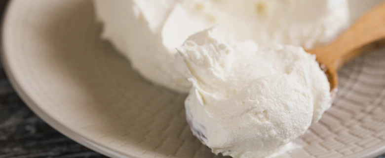 Bílá krémová hmota na dřevěném lžíci, podobná mascarpone