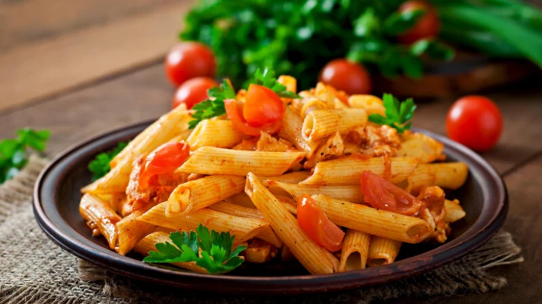 Penne s kuřecím masem a rajčaty na tmavém talíři