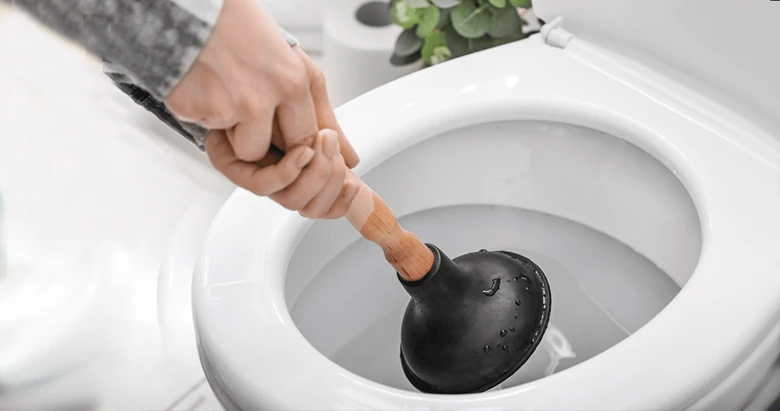 Ruka s hadicí čistící záchod od zácpy.