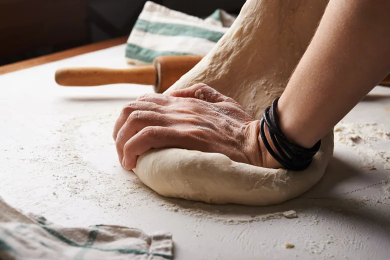 Ruce tlačí kynuté těsto na pizzu na moučném povrchu
