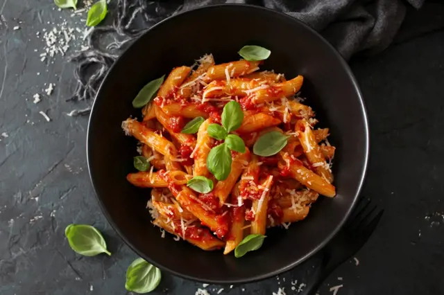 Pasta s rajčatovou omáčkou a bazalkou v černém talíři