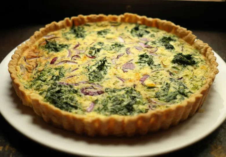 Zeleninová quiche se špenátem a cibulí na bílém talíři.
