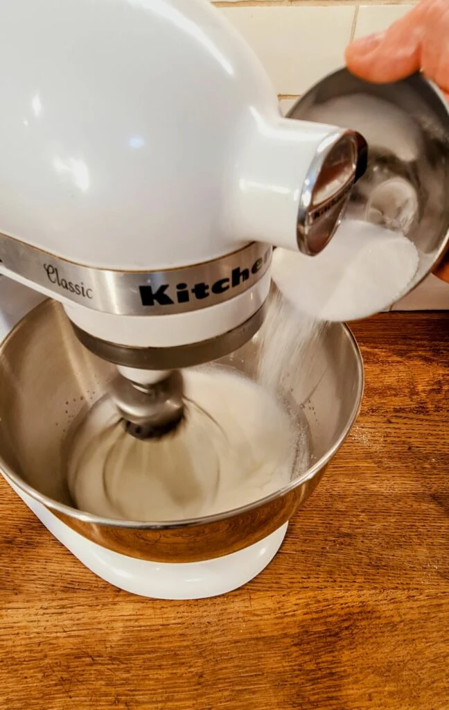 Přisypaní cukru do mísy mixéru při šlehání těsta na dort.