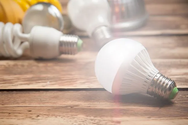 Různé typy žárovek na dřevěném stole – LED a úsporné žárovky