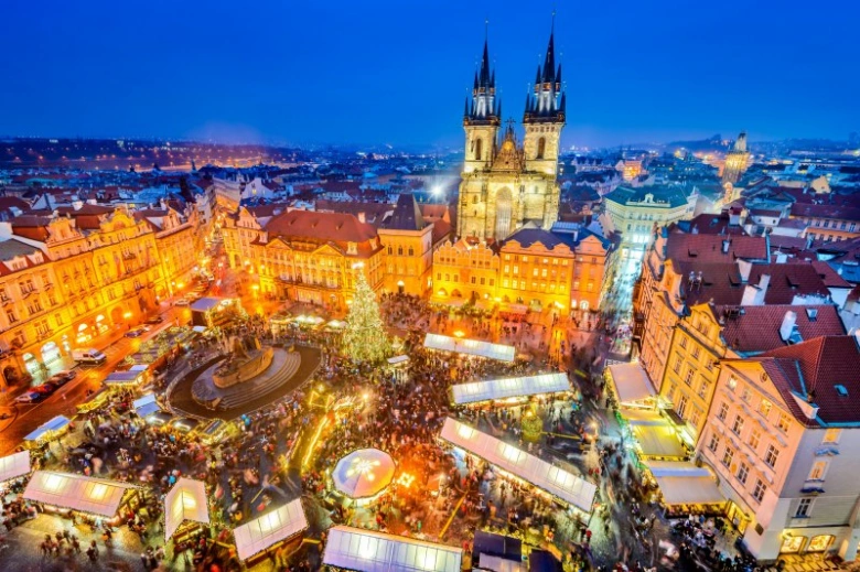 Vánoční trhy na Staroměstském náměstí v Praze s osvětlenými stánky a kostelem Panny Marie před Týnem