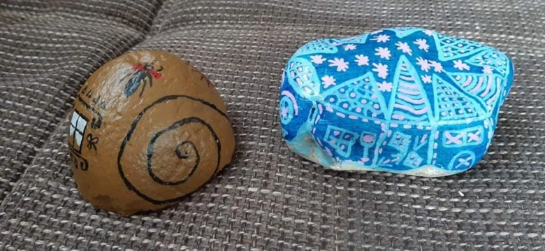 Dva namalované kameny s kreativními motivy – ušlechtilý šnečí dům a modrý geometrický vzor