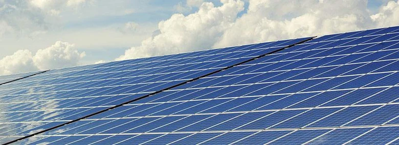 Modré fotovoltaické panely na střeše pod oblohou s mraky.