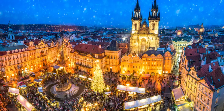 Vánoční trhy na Staroměstském náměstí v Praze s osvětleným stromem a kostelem Panny Marie před Týnem