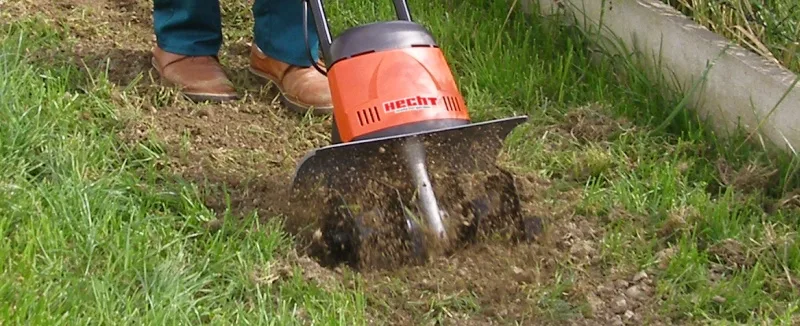 Osoba používá oranžový kultivátor pro zpracování půdy.