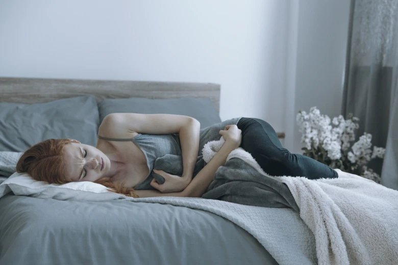 Žena ležící v posteli s bolestí žaludku a pocitem na zvracení