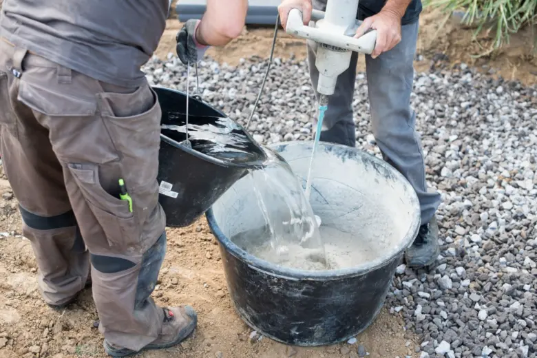 Pracovníci míchají beton v kbelíku pomocí ručního mixéru
