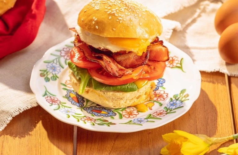 Delikátní hamburger s vejcem, slaninou a rajčaty na ozdobném talíři.