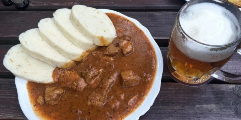 Guláš s chlebem a pivem na dřevěném stole