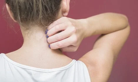 Žena si škrábe záda u krku kvůli svědění kůže