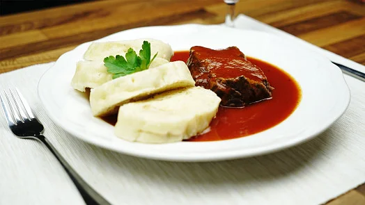 Houskové knedlíky s gulášem na bílém talíři