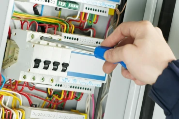 Elektrikář upravuje komponentu v rozvaděči šroubovákem.