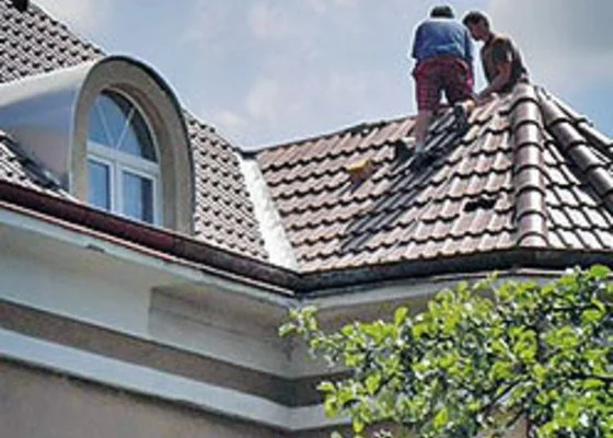 Dva dělníci opravují střechu domu s taškami.