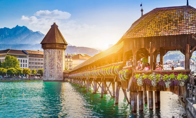 Mostní kaple ve švýcarském Luzernu s věží na pozadí hor.