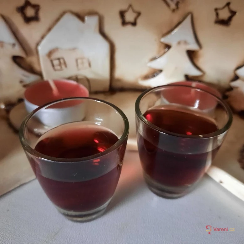Domácí likér z aronie v skleničkách na vánočním pozadí.